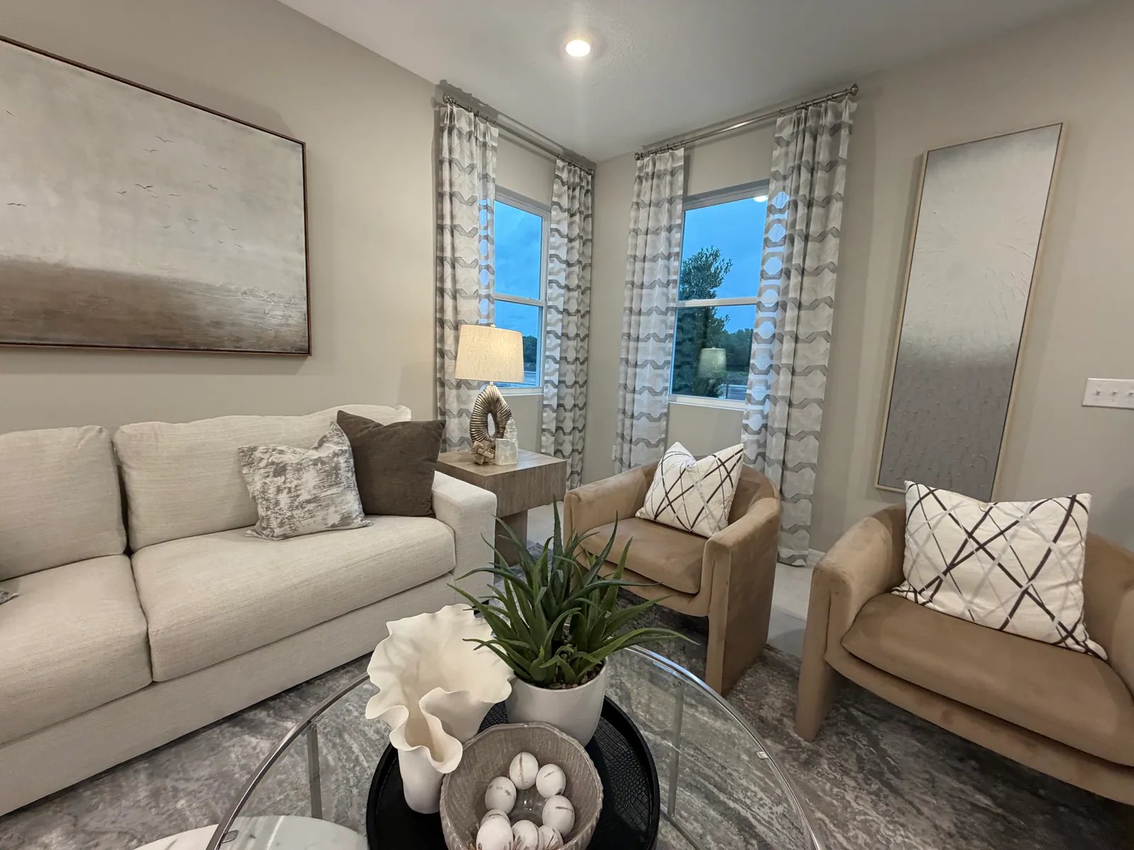 Sala con sofá claro, dos butacas y ventanas con cortinas